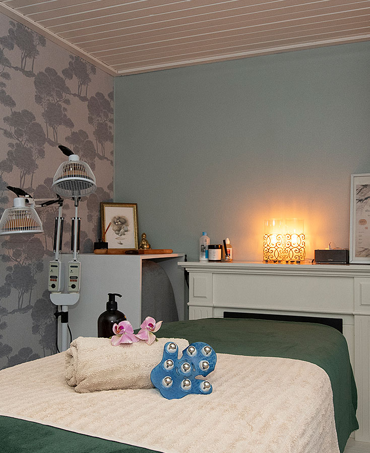 Behandelruimte van Studio Flow Feel & Create met een massagebank, opgevouwen handdoek met bloem, warme groene tinten en een serene, ontspannen sfeer